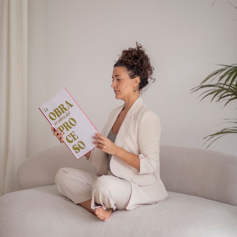 Laurie Ce. coach creativa sentada en un sofá ojeando su folleto "la obra es sobra del proceso"
