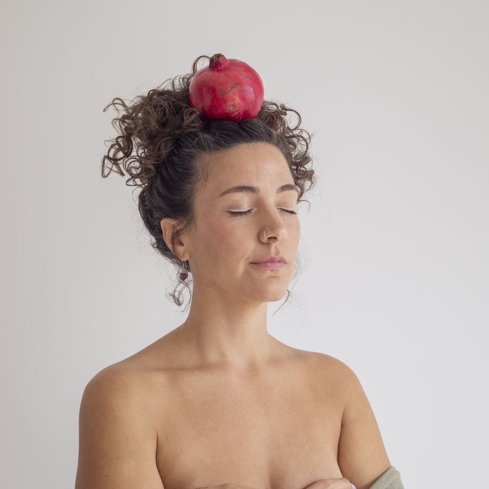 Laura Ce. coach creativa sosteniendo una granada en su cabeza con los ojos cerrados.