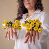 Manos de Laura, coach creativa, con flores amarillas saliendo de la manga de la camisa y las uñas malva.